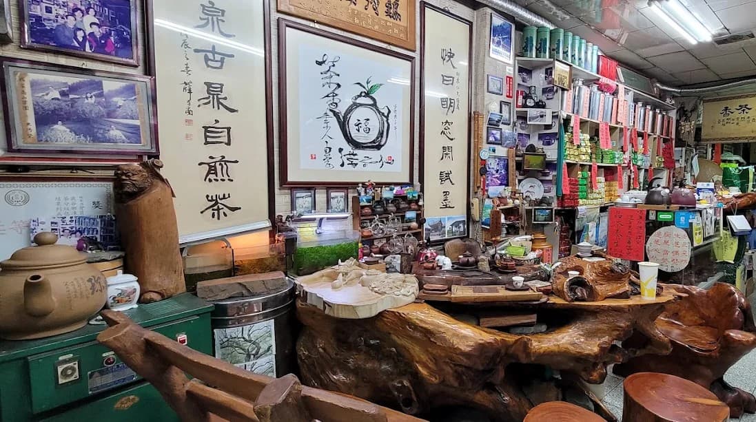 店內全景：牆上掛滿書法字畫與老照片，中央是整塊樹根雕成的大茶桌，右側木架上排列成排的錫製茶罐與茶具
